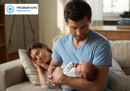 Мужчина держит на руках младенца, рядом спит женщина